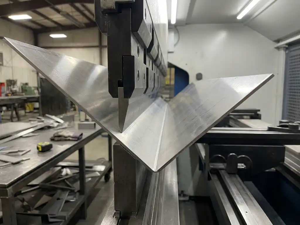 CNC kantpers vormt scherpe hoekige plooi in geborsteld roestvrij staal, industriële werkplaats met zacht diffuus licht op de achtergrond.